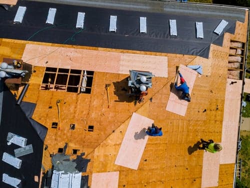 Aerial view of a Roofing abc crew replacing a roof, decking exposed and underlayment going down